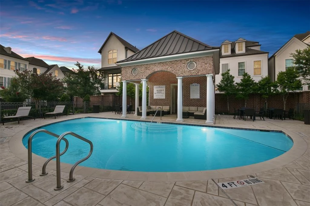 Community swimming pool at dusk with a covered seating area and surrounding homes.
