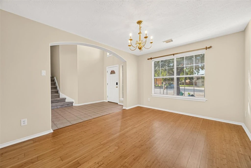 Original empty dining room with wood flooring, a chandelier, a large window, and an archway to the entry.