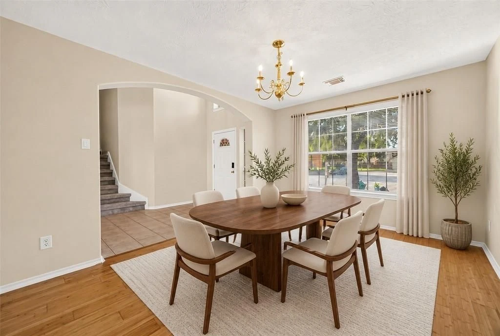 Virtually staged dining room with a digitally added wooden table, chairs, rug, curtains, plants, and tabletop décor.